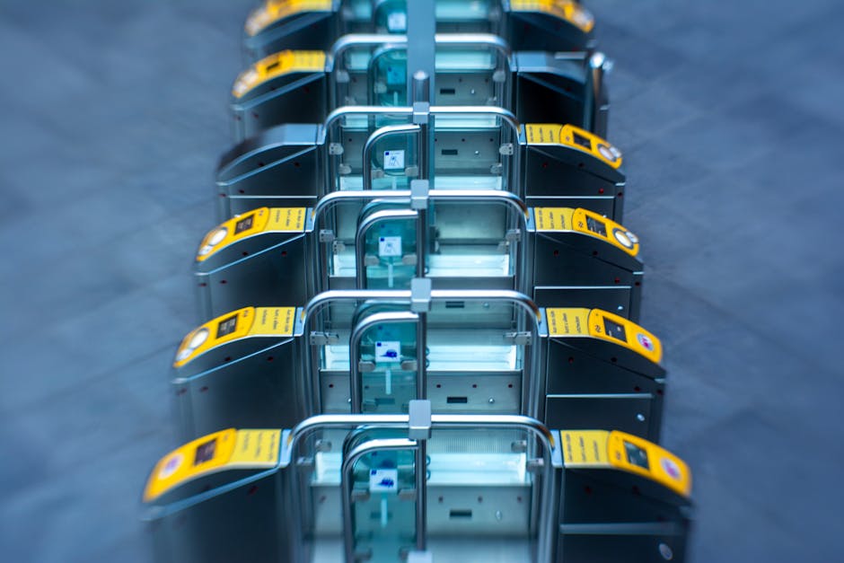 Close-up view of a section of pavement at a train or bus station, featuring a tactile yellow warning strip with raised circular studs designed for visually impaired pedestrians. The tactile surface is
